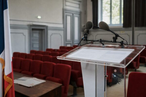 Salle de presse française vide avec pupitre, micros et drapeau tricolore discret pour illustrer le débat de Raphaël Glucksmann sur l’immigration et le service civique.