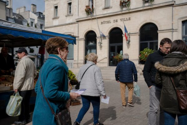 Scène de marché dans une ville moyenne française avec habitants anonymes près d’un bâtiment public local.