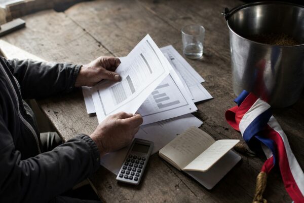 Flat lay photojournalistic d’un dossier parlementaire agricole sur une table de ferme, avec écharpe tricolore pliée et matériel d’élevage.