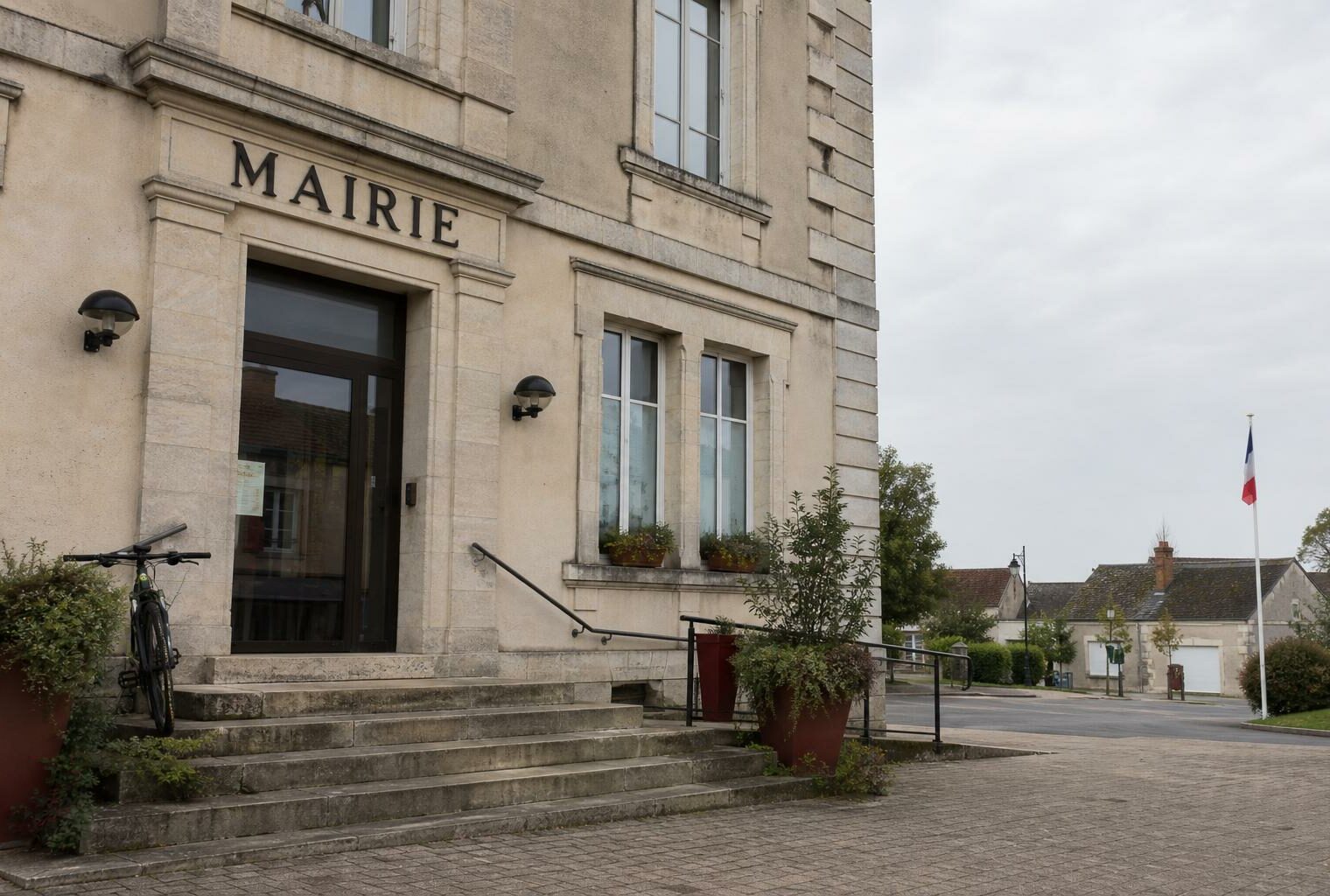 Façade d’une mairie de petite commune française, avec drapeau tricolore discret et square vide, illustration du débat sur le cumul des mandats.