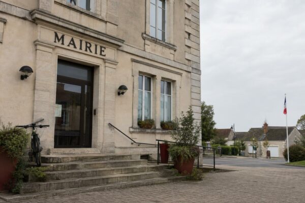 Façade d’une mairie de petite commune française, avec drapeau tricolore discret et square vide, illustration du débat sur le cumul des mandats.