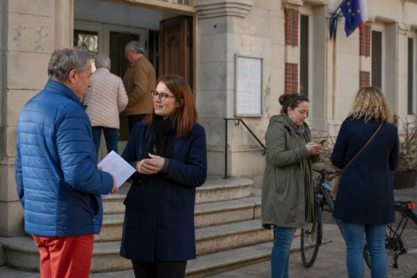 Des citoyens discutent devant une mairie de quartier, dans une scène de vie civique française en plein jour.