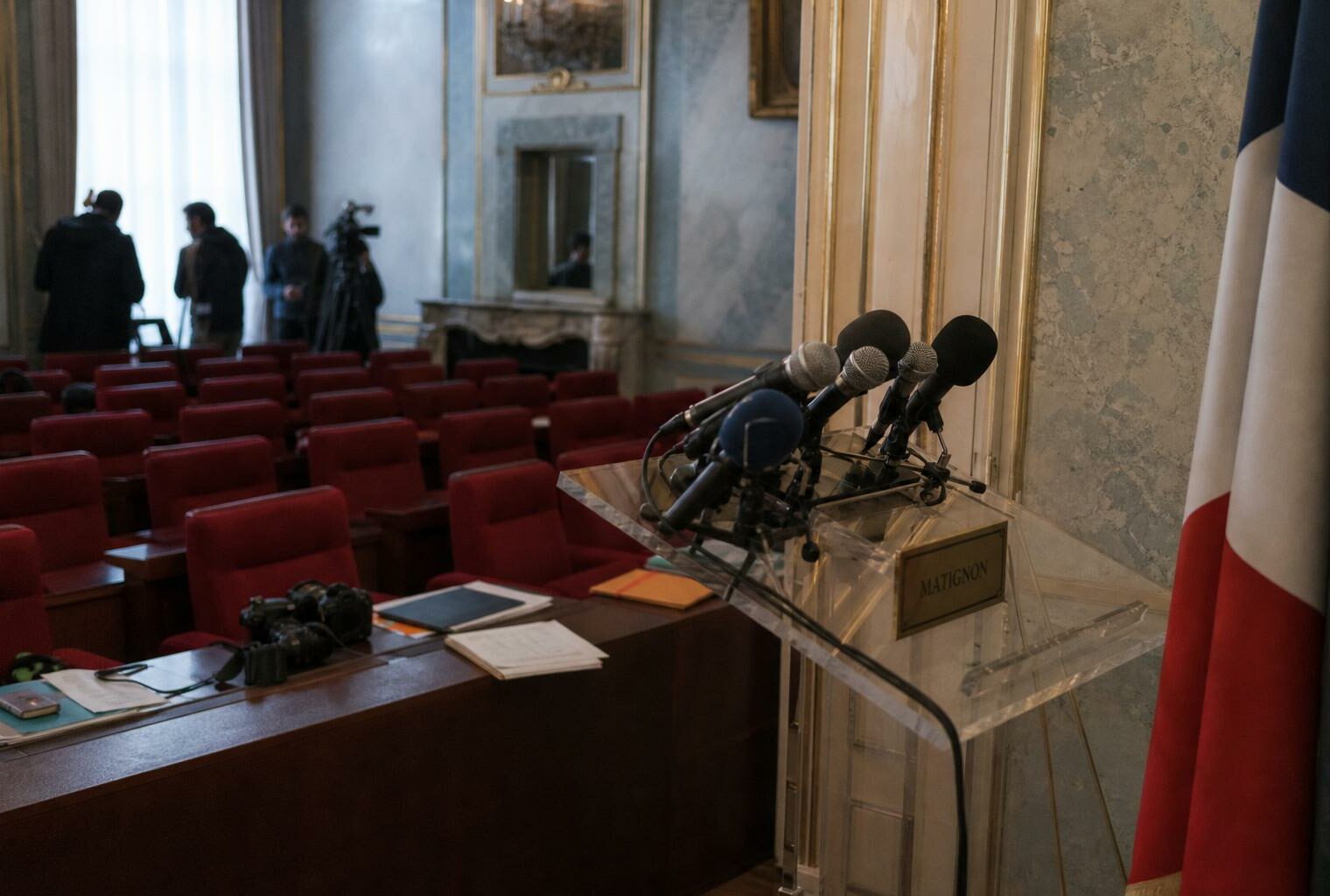 Salle de presse de Matignon avec pupitre vide, micros et drapeau tricolore discret, ambiance de conférence de presse gouvernementale