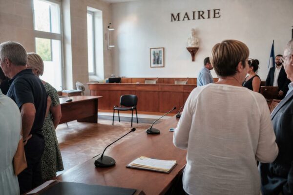 Salle municipale française lumineuse avec micros, dossiers flous et chaise vide lors d’un rendez-vous politique.