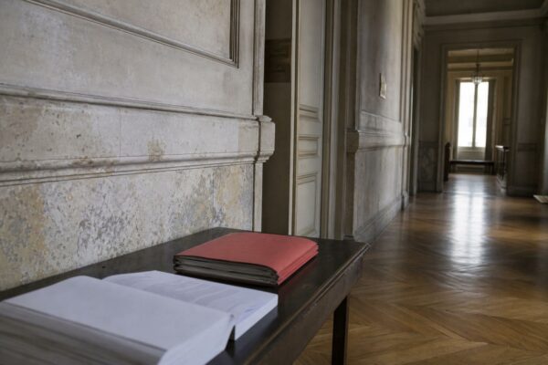 Couloir institutionnel parisien avec dossier rouge et code juridique, illustrant le débat sur l’état d’urgence contre le narcotrafic.
