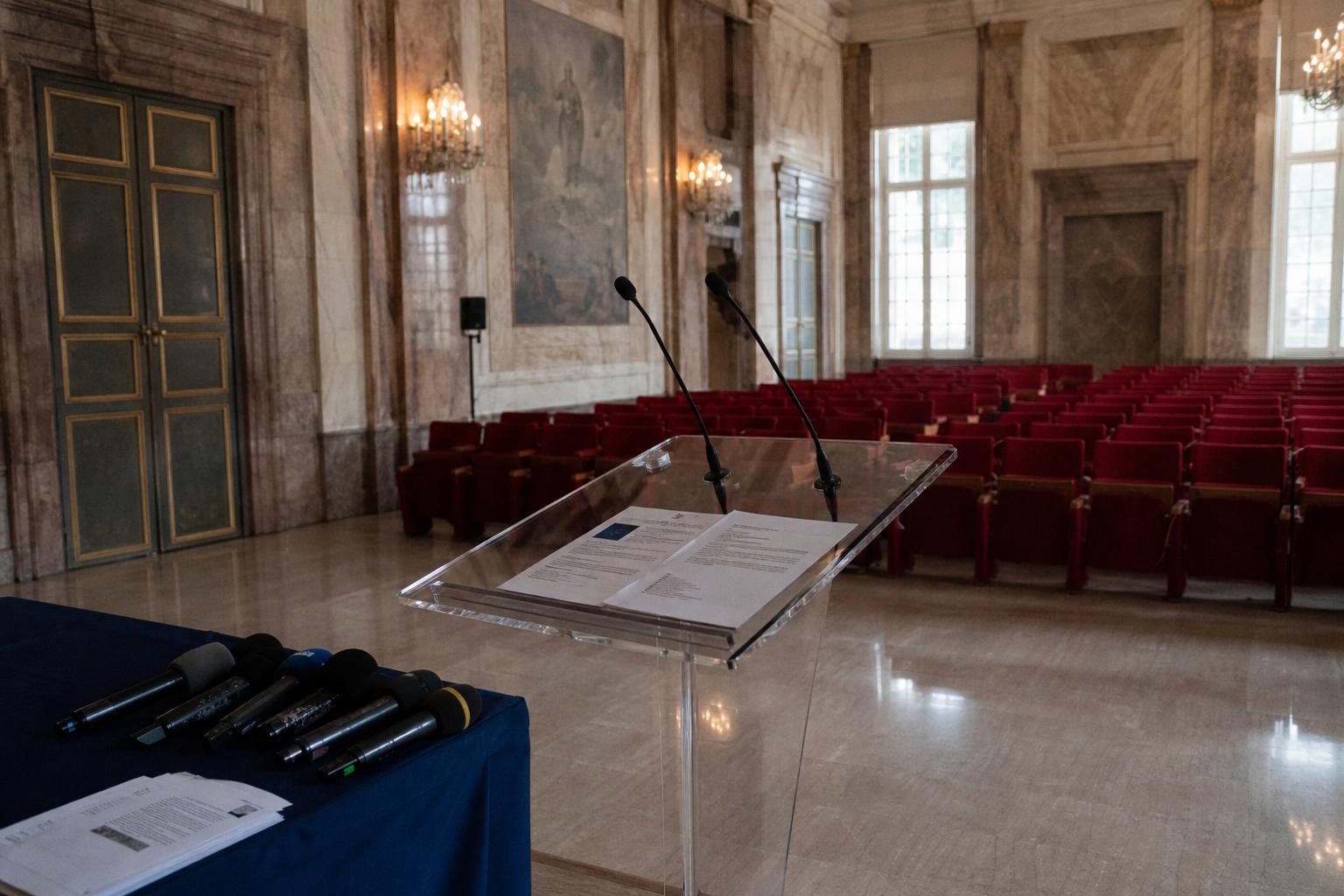 Salle de presse gouvernementale vide à Matignon avec pupitre, micros et sièges rouges, ambiance institutionnelle sobre.