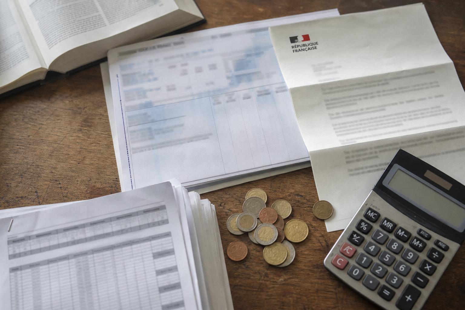 Vue en plongée d’un bureau avec fiche de paie, calculatrice, pièces en euros et document officiel français flouté sur les négociations salariales.