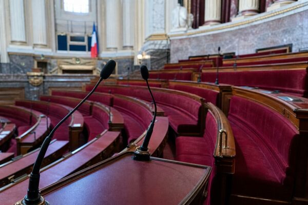 Intérieur vide du Sénat avec sièges rouges et pupitre, illustrant le débat sur la session extraordinaire