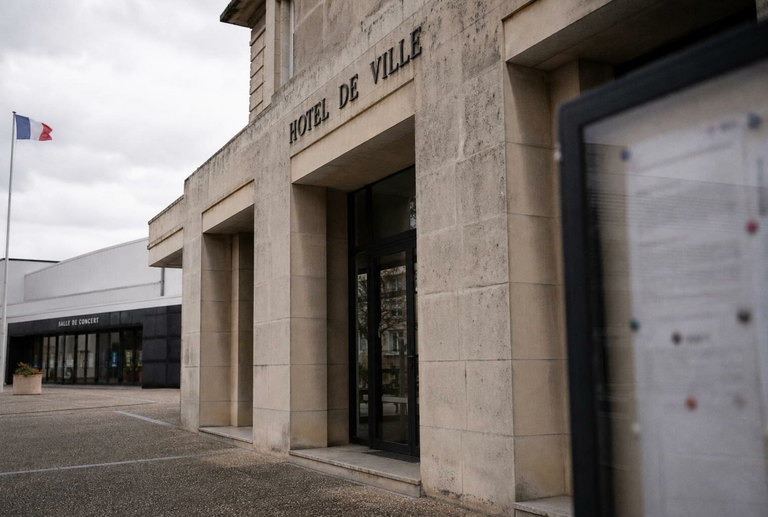 Façade d’une mairie française près d’une salle de concert, avec drapeau tricolore discret et ambiance éditoriale neutre.