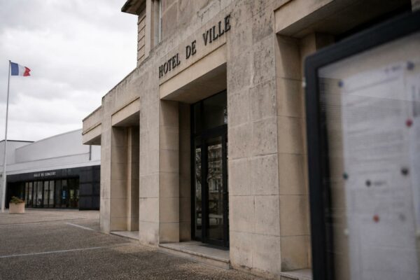 Façade d’une mairie française près d’une salle de concert, avec drapeau tricolore discret et ambiance éditoriale neutre.