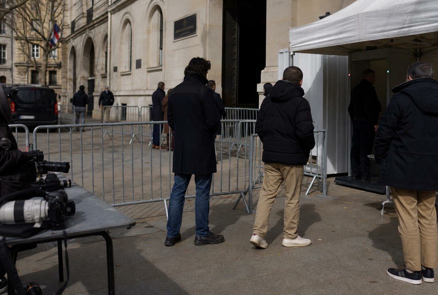 Périmètre de sécurité calme devant un bâtiment judiciaire parisien, silhouettes anonymes et barrières fermées.
