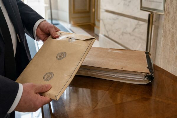 Main d’enquêteur avec dossier et enveloppe scellée dans un couloir lumineux de l’Élysée