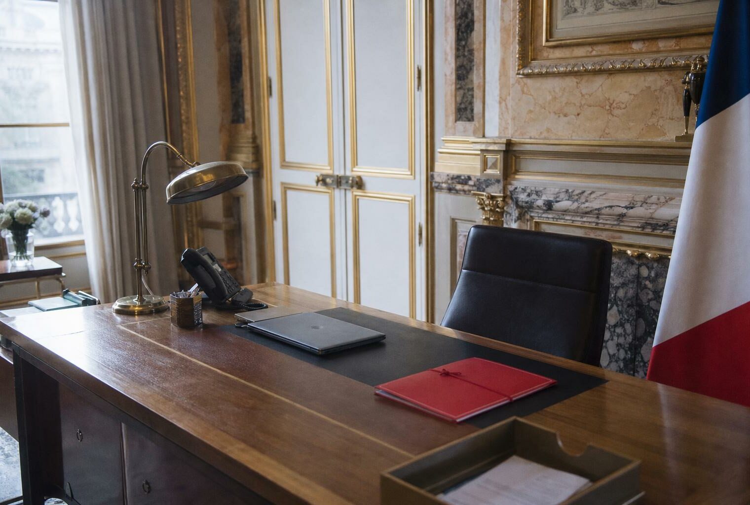 Bureau présidentiel vide à l’Élysée avec dossier fermé et drapeau tricolore partiel, ambiance institutionnelle photographiée en plan large.