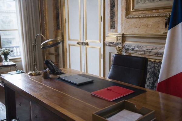 Bureau présidentiel vide à l’Élysée avec dossier fermé et drapeau tricolore partiel, ambiance institutionnelle photographiée en plan large.