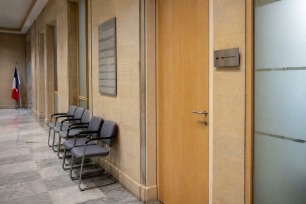 Couloir clair d’une institution française, porte close et chaises vides, ambiance sobre sur le pouvoir politique.