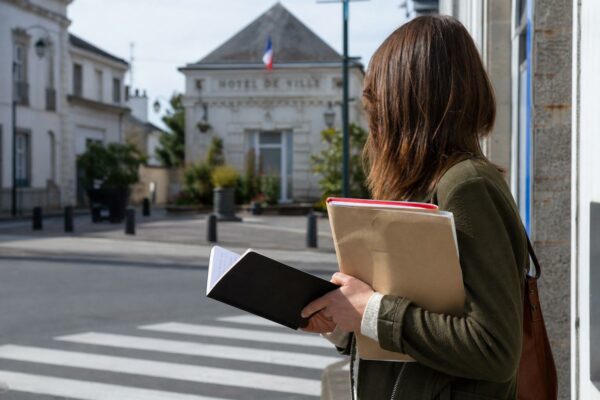 Portrait d’un jeune collaborateur anonyme avec carnet devant une mairie de province
