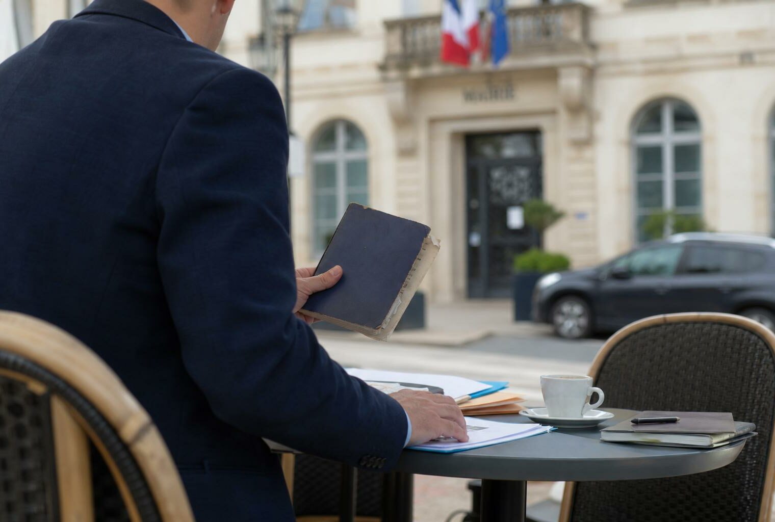 Un élu local anonyme consulte un carnet devant une mairie française, dans une scène de campagne sobre et naturelle.