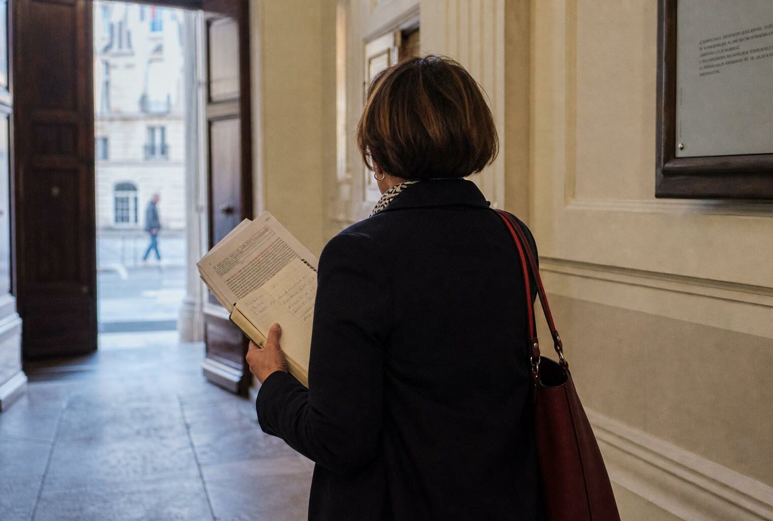 Un collaborateur municipal de dos tient un dossier dans un couloir de mairie, avec la rue en arrière-plan flou.