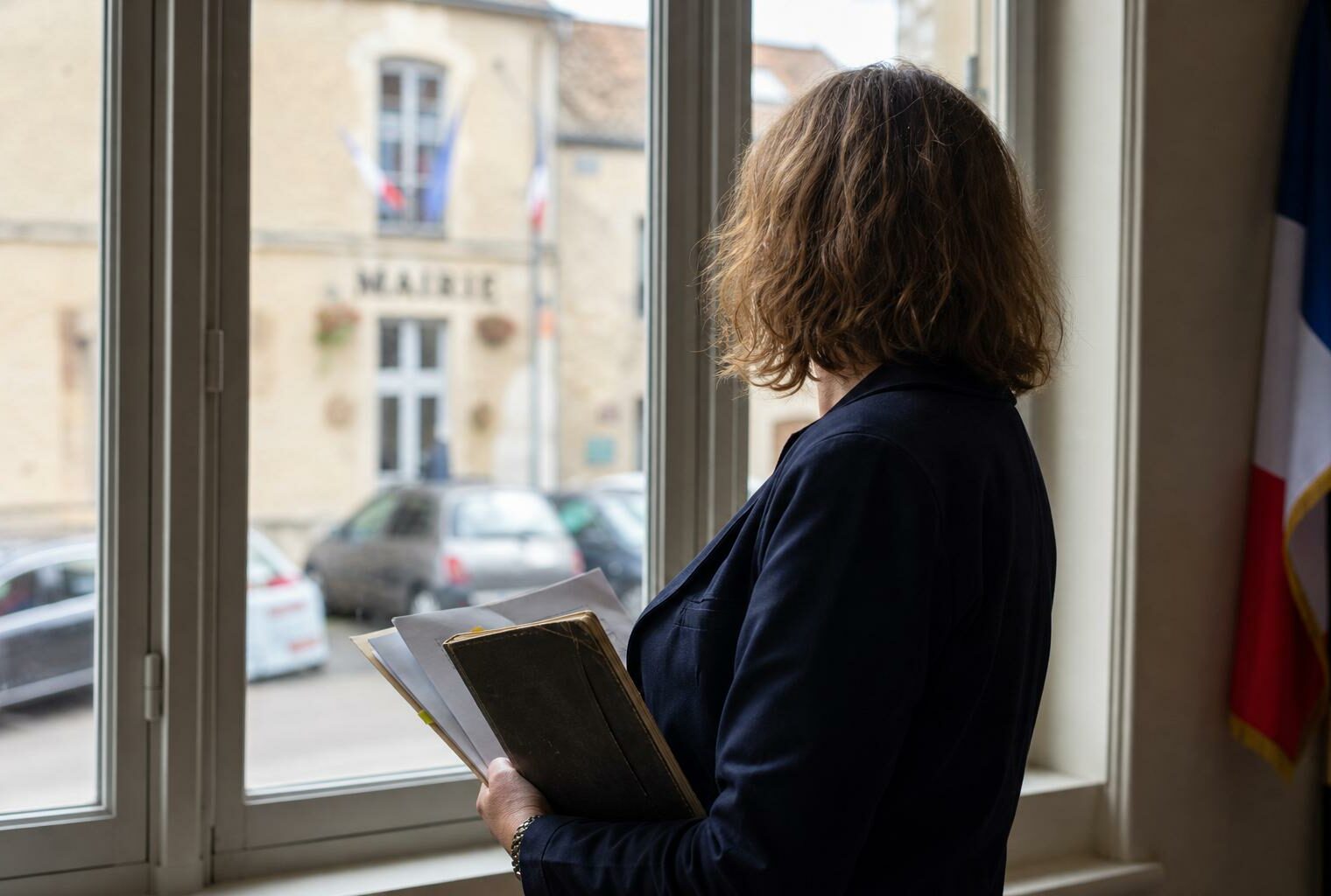 Portrait photojournalistique d’un élu local de dos dans une mairie française, carnet en main, lumière naturelle