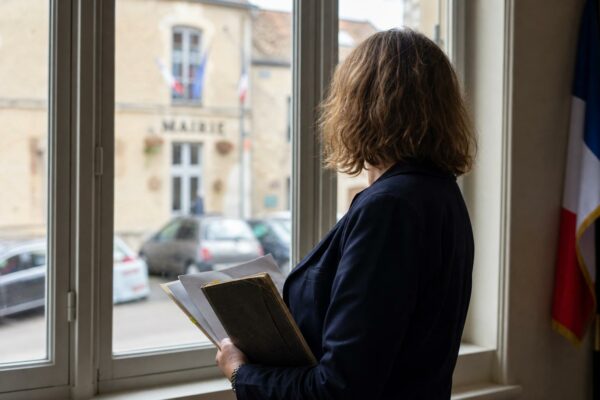 Portrait photojournalistique d’un élu local de dos dans une mairie française, carnet en main, lumière naturelle