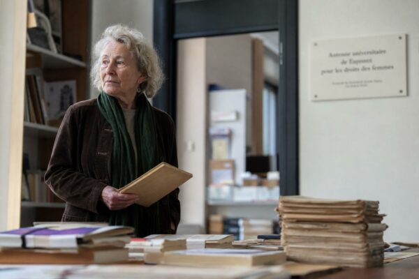 Portrait éditorial d’une militante féministe française dans une salle d’archives, avec dossiers et livres anciens, lumière naturelle et ambiance de presse.