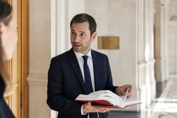 Portrait d’un juriste français dans un couloir de palais de justice, tenant un code de loi ouvert.