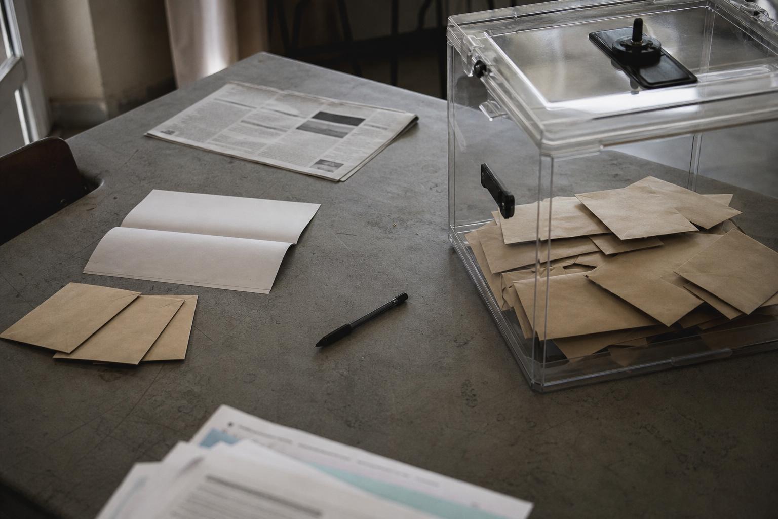 Vue de table de réunion politique avec urne transparente, documents flous et ambiance éditoriale neutre pour illustrer la primaire de gauche 2027