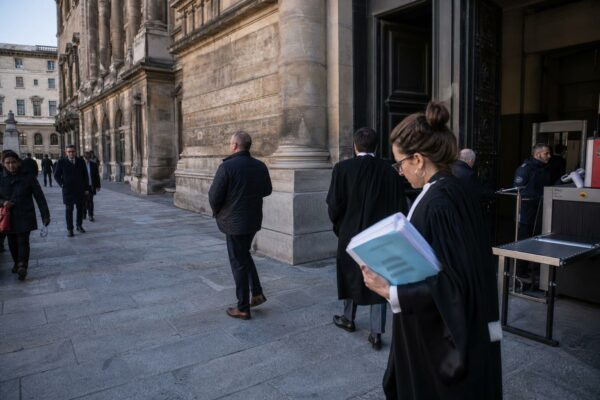 Devant un palais de justice parisien, des avocats et passants anonymes traversent une entrée de cour calme.