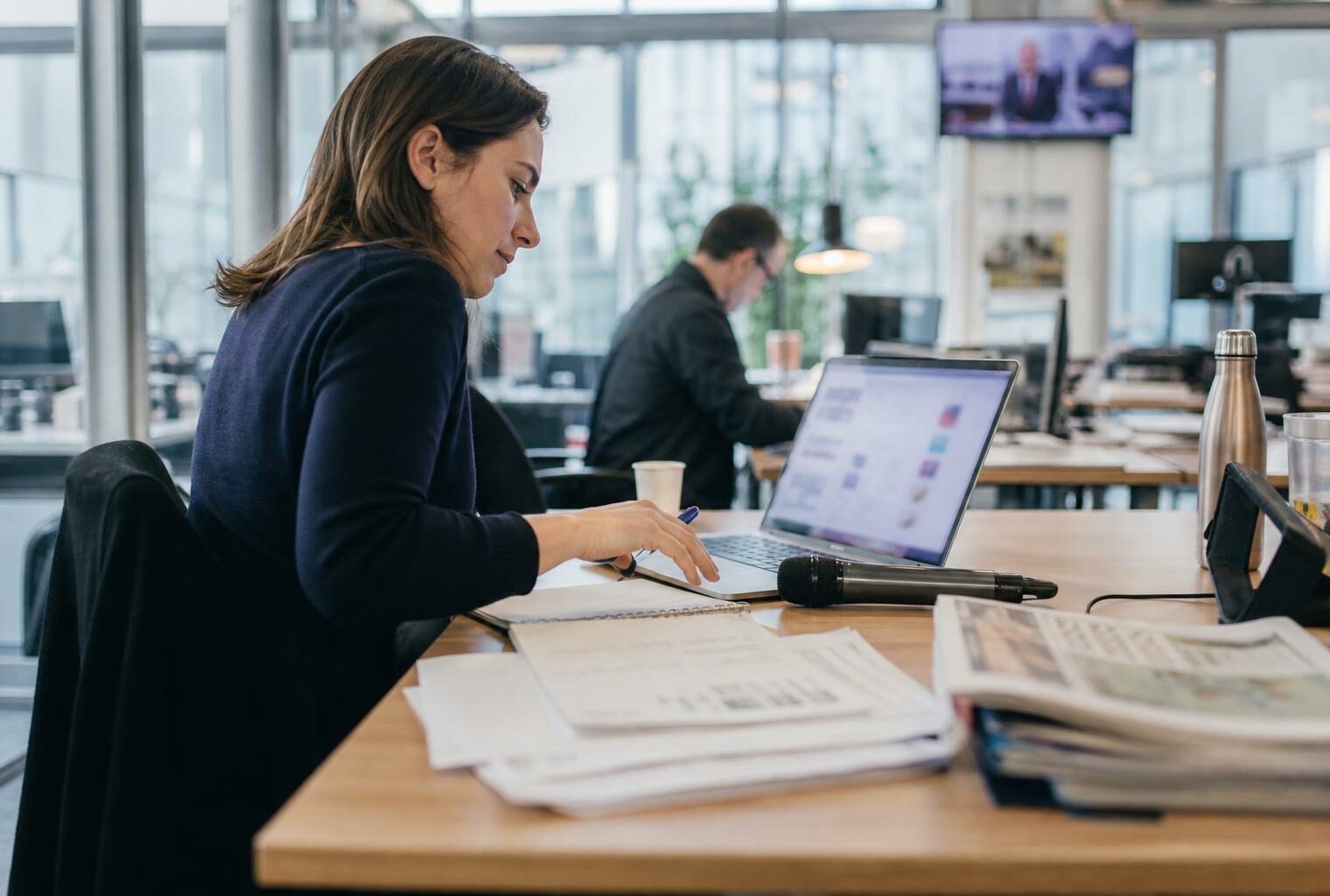 Rédaction française en pleine réunion, avec micro sans logo, écran flou et piles de documents