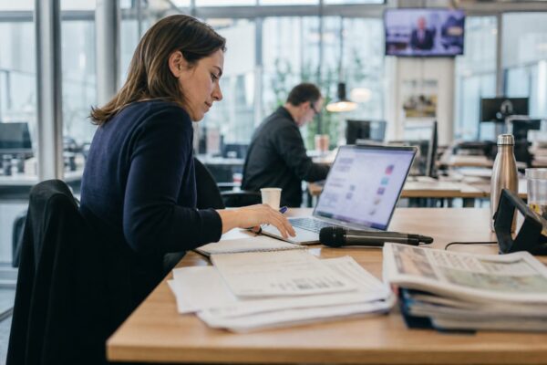 Rédaction française en pleine réunion, avec micro sans logo, écran flou et piles de documents