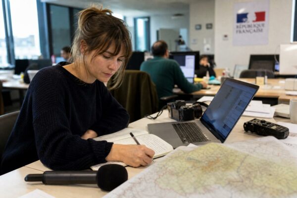 Journaliste en rédaction préparant un sujet territorial avec carnet, micro sans logo et carte papier floue.