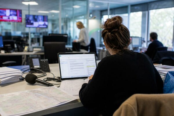Journaliste préparant un sujet territorial dans une rédaction française, avec carnet, micro sans logo et carte floue.