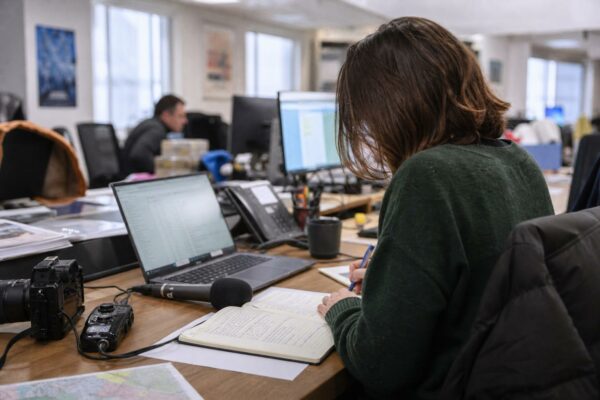 Journaliste en rédaction locale préparant un dossier politique avec carnet, micro sans logo et carte papier floue.