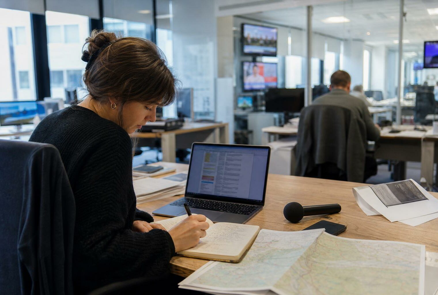 Journaliste en rédaction locale préparant un sujet sur la protection de l’enfance, avec carnet, micro et écran flou.