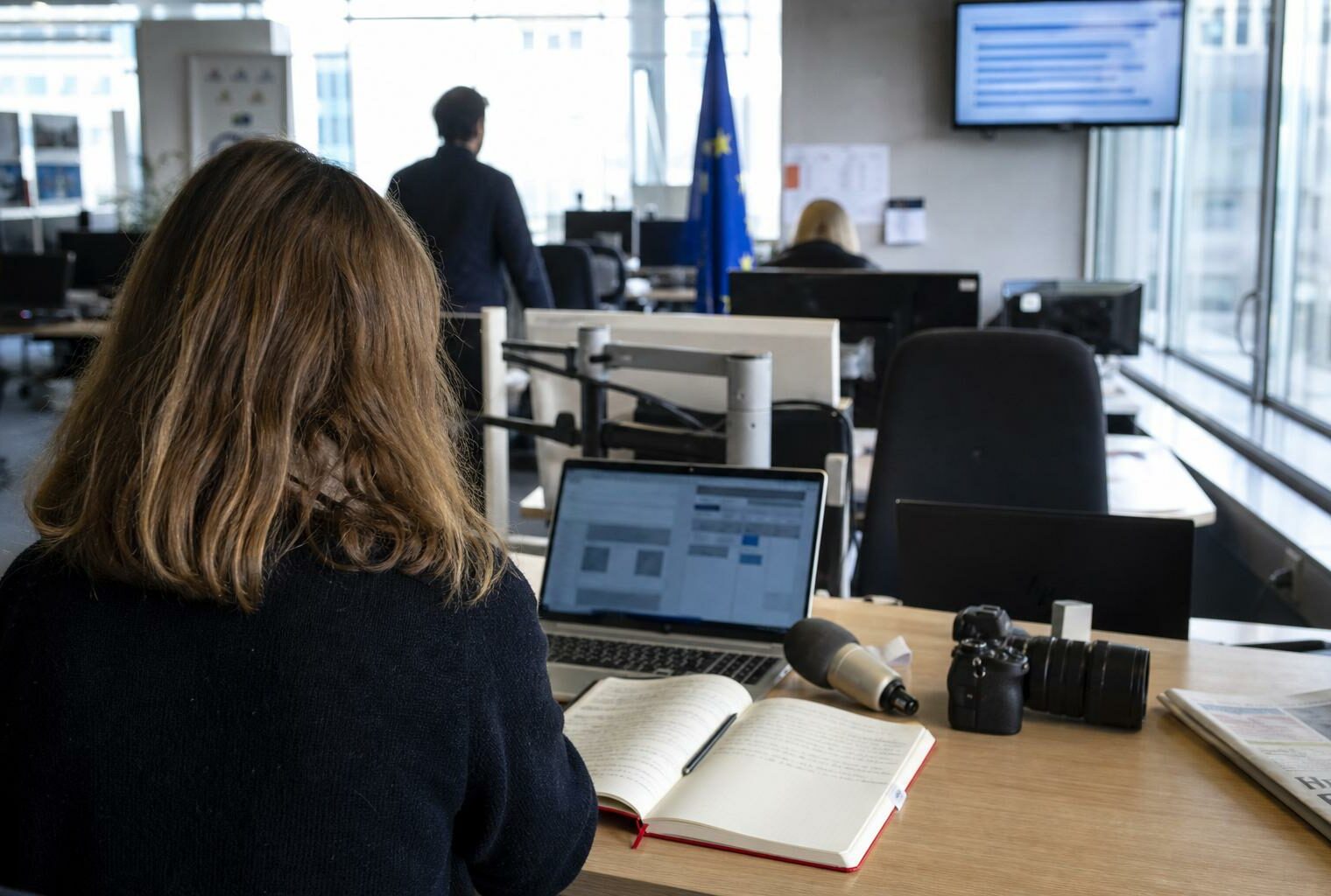 Rédaction française avec journaliste, micro sans logo et écrans flous préparant un sujet sur le Parlement européen.