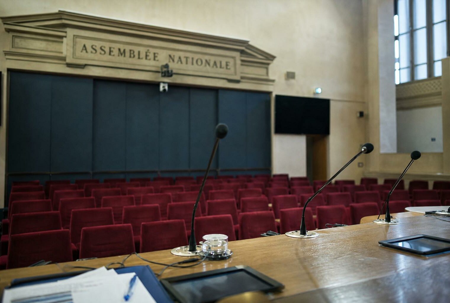 Salle de presse vide à l’Assemblée nationale avec pupitre, micros et sièges rouges pour illustrer le flou du RN sur les retraites.