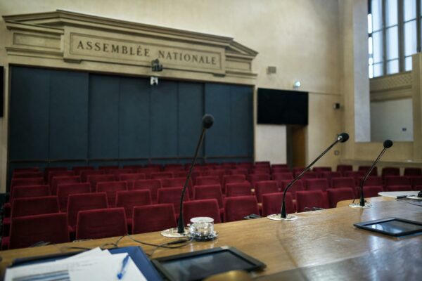 Salle de presse vide à l’Assemblée nationale avec pupitre, micros et sièges rouges pour illustrer le flou du RN sur les retraites.