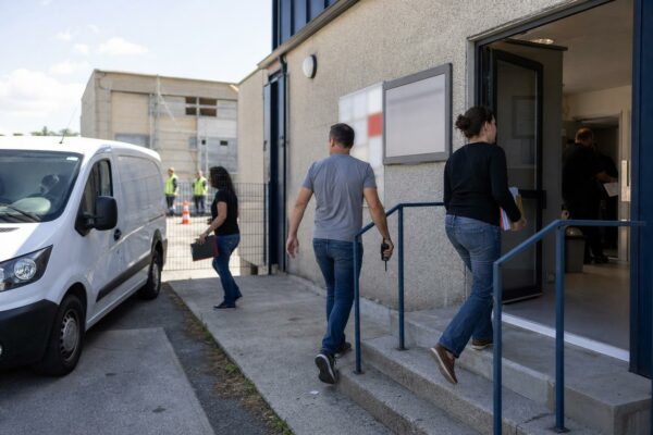 Scène de terrain calme devant un bâtiment français de sécurité civile, avec personnels anonymes et véhicule non marqué.