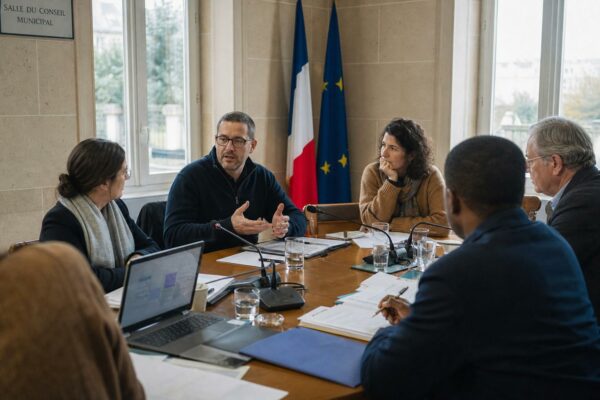 Réunion sur le logement dans une mairie française, avec plusieurs participants anonymes autour d’une table et des micros de presse.