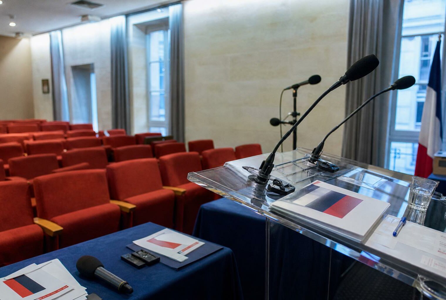 Salle de presse politique vide avec pupitre, micros et drapeau tricolore discret
