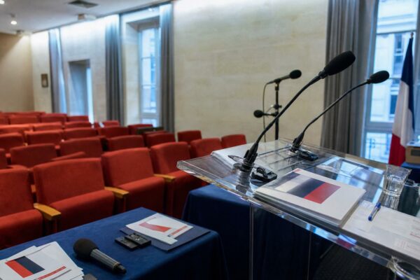 Salle de presse politique vide avec pupitre, micros et drapeau tricolore discret
