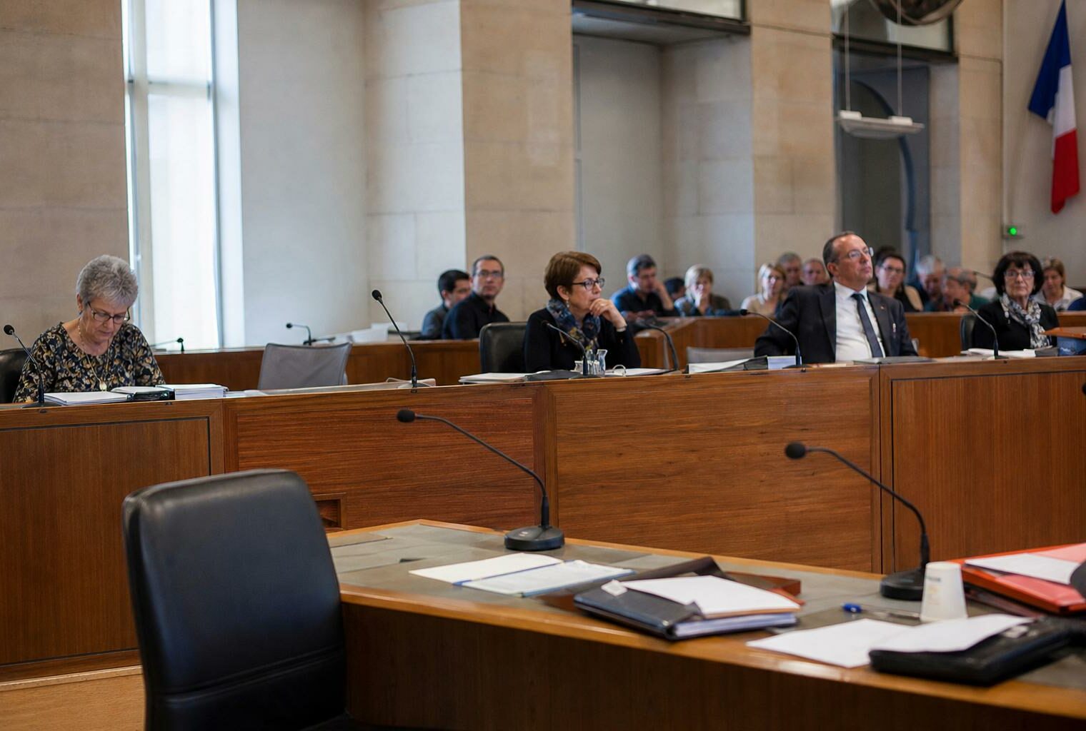 Salle du conseil municipal lumineuse avec chaise vide, micros et dossiers flous dans une mairie française.