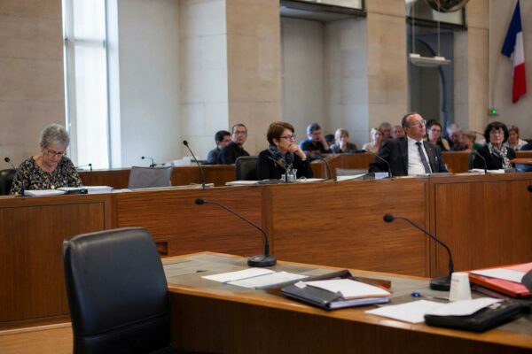 Salle du conseil municipal lumineuse avec chaise vide, micros et dossiers flous dans une mairie française.