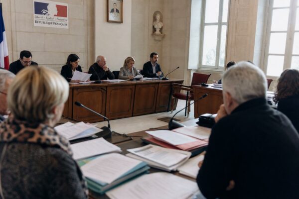 Salle municipale lumineuse avec chaise vide, micros de réunion et dossiers flous lors d’un conseil local