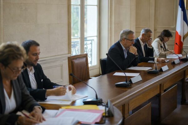 Salle municipale française avec chaise vide, micros et dossiers flous pour illustrer la protection de l’enfance.