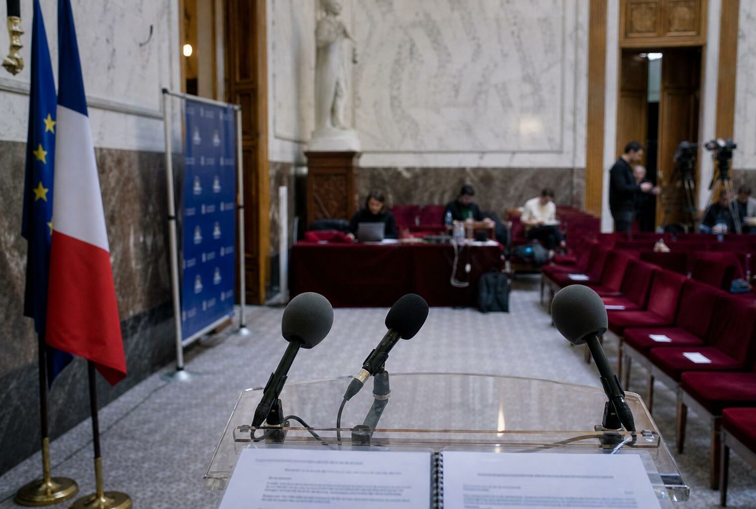 Salle de presse du Sénat avec pupitre vide, micros de presse et rangées de sièges rouges avant un débat sur le protoxyde d’azote et les rave-parties.