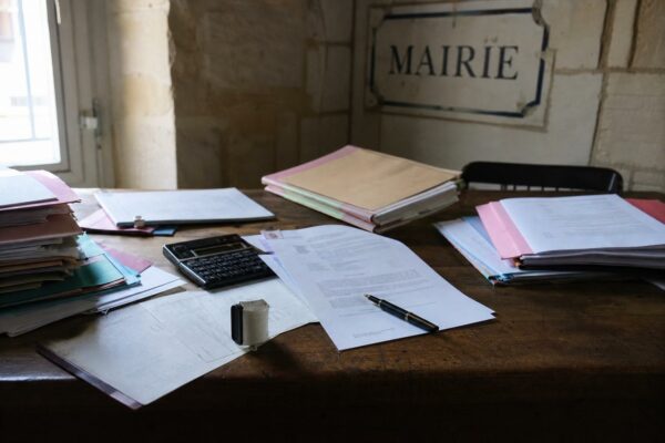 Bureau de mairie avec dossiers administratifs, tampon et plaque MAIRIE floue, illustrant la simplification des normes.