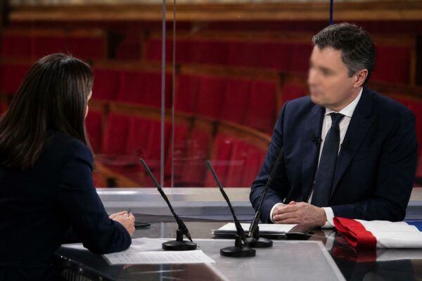 Deux responsables politiques anonymes en interview télévisée, avec micros de presse et drapeau tricolore discret en arrière-plan.
