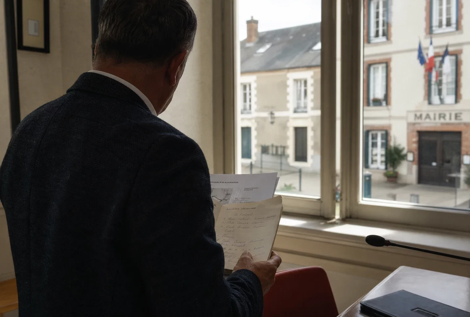 Collaborateur de mairie de dos avec dossier, dans un intérieur civique français lumineux en lien avec l’A69.
