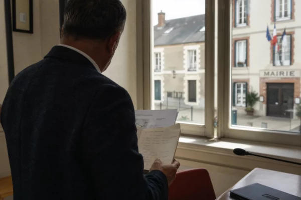 Collaborateur de mairie de dos avec dossier, dans un intérieur civique français lumineux en lien avec l’A69.